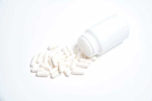 Beyaz arka planda hapların yazıları olmayan beyaz plastik tüp ve yanında beyaz haplar.