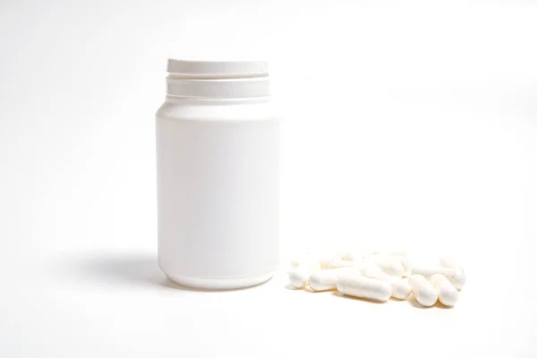 Beyaz arka planda hapların yazıları olmayan beyaz plastik tüp ve yanında beyaz haplar.