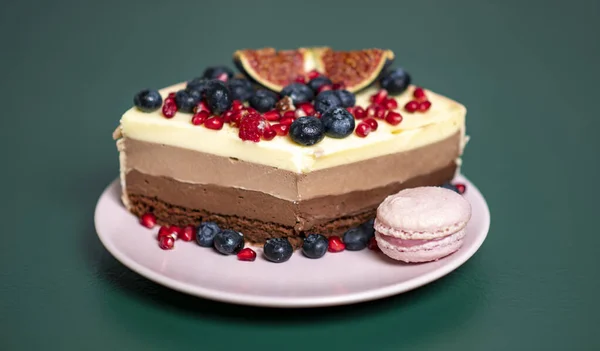 Pembe tabakta bir parça kek, taze böğürtlen ve badem kurabiyesi koyu yeşil arka planda bir fincan çay.