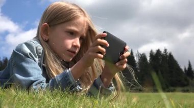 4k kız portre oynarken Tablet, çayır çimen Park Smartphone kullanarak çocuk