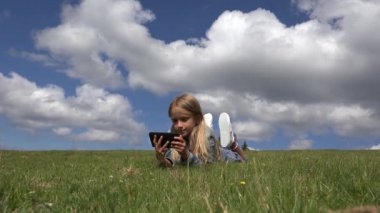 Çocuk oynamaya Tablet açık park, çayır çimen 4 k Smartphone kullanan kız