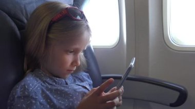 4 k kız oynamaya Tablet düzlemde, uçağın içinde akıllı telefonlar kullanarak çocuk portre