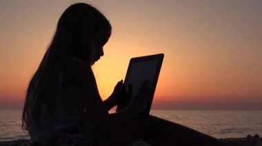 Kumsalda, Sunset View çocuk siluet akıllı telefonlar 4 k kullanarak tablet oynayan kız