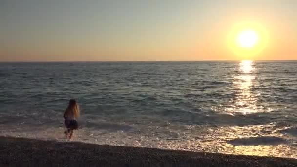 在日落的海滩上玩耍的女孩 快乐的孩子漫步在海边的海浪中 — 图库视频影像