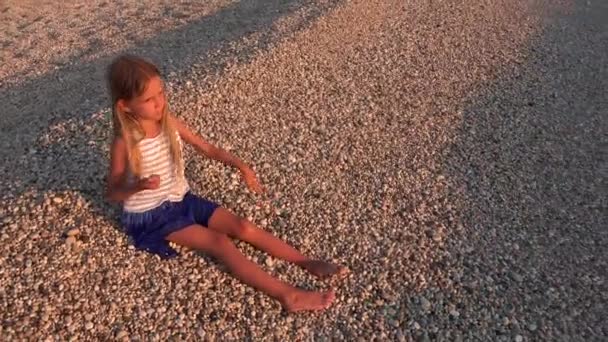 で小石を投げて笑顔の子に日没でビーチで遊ぶ女の子 — ストック動画