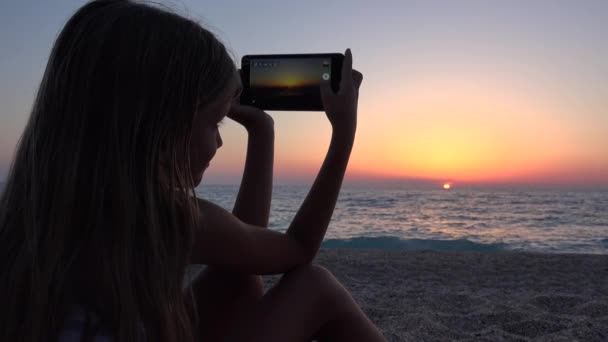 Dziewczyna Plaży Zachodzie Słońca Dziecko Pomocą Inteligentnego Telefonu Robienia Zdjęć — Wideo stockowe