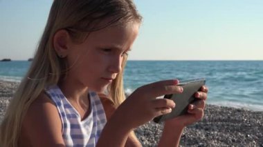 4 k kız oynamaya tablete Beach, Sunset View, çocuk kullanarak akıllı telefon, deniz kıyısı