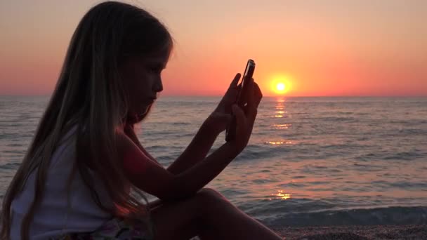 Chica Jugando Tableta Playa Atardecer Niño Usando Teléfono Inteligente Orilla — Vídeos de Stock