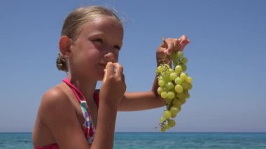 Çocuk portre kumsalda, kız yüz üzüm yemek meyve Seashore 4 k yiyor.