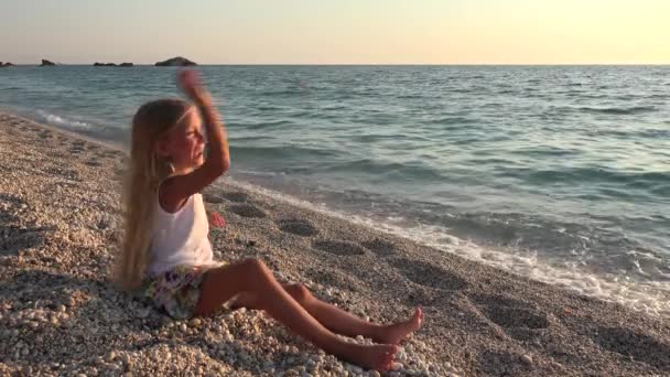 再生ビーチの日没で笑顔の子海の水に小石を投げて 女の子 — ストック動画