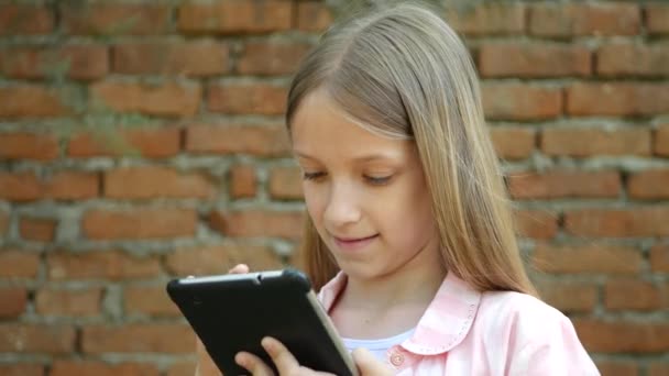 孩子玩平板砖墙在院子里 小女孩使用智能手机户外 — 图库视频影像