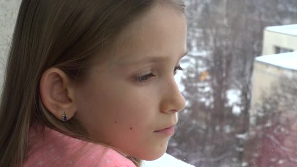 悲しい子ウィンドウで 不幸な思いやりのある女の子の顔 雪が降る冬の日 を探して — ストック動画