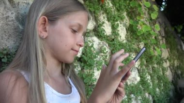 Taş duvar tarafından Smartphone bahçede, küçük kız oynayan çocuk Tablet açık kullanır