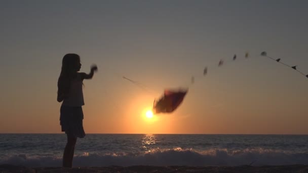 Enfant jouant au cerf-volant volant sur la plage au coucher du soleil, joyeuse petite fille sur la côte 