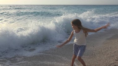 Kumsalda oynarken, deniz dalgaları, seyretmekten çocuk yaz aylarında kıyı şeridi üzerinde koşan kız