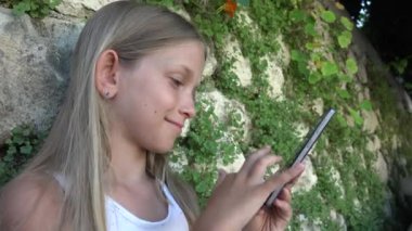 Taş duvar tarafından Smartphone bahçede, küçük kız oynayan çocuk Tablet açık kullanır
