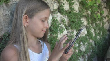 Taş duvar tarafından Smartphone bahçede, küçük kız oynayan çocuk Tablet açık kullanır