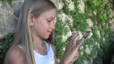 Taş duvar tarafından Smartphone bahçede, küçük kız oynayan çocuk Tablet açık kullanır