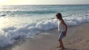 Kumsalda oynarken, deniz dalgaları, seyretmekten çocuk yaz aylarında kıyı şeridi üzerinde koşan kız