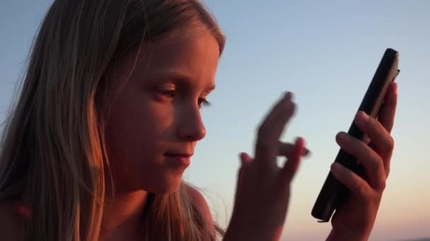 子供の遊びスマートフォン 日没のビーチで子供 海岸でタブレットを使用して女の子 — ストック動画