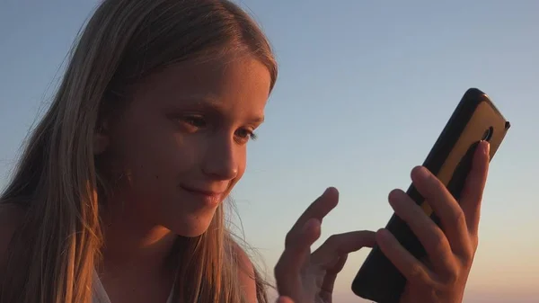 子供の遊びスマートフォン 日没のビーチで子供 海岸でタブレットを使用して女の子 — ストック写真