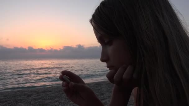 Dítě na pláži, chlapče, hraje na břehu v západu slunce, dívka sledování studiem oblázky