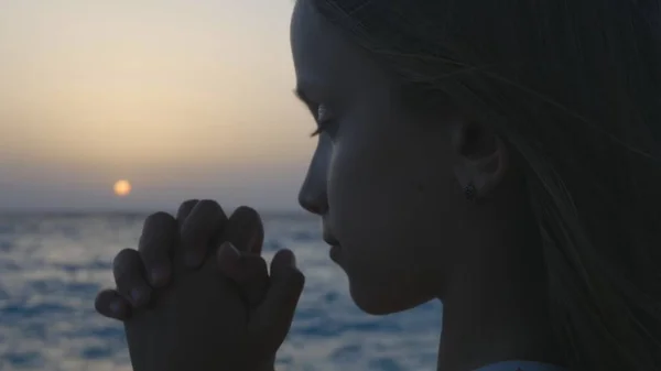 Kind bidden op strand bij zonsondergang, doordachte gebed Kid, nadenkend meisje op zee — Stockfoto