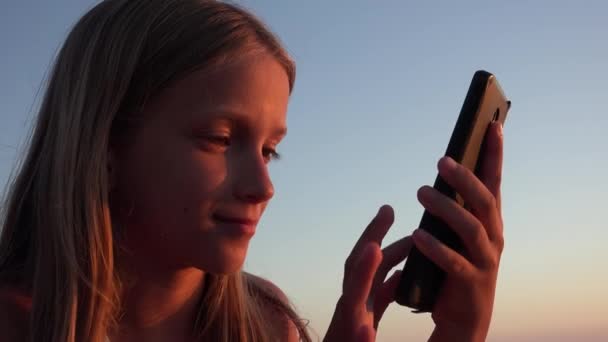 Barnlek Smartphone, Kid på stranden vid solnedgången, Flicka med surfplatta på stranden — Stockvideo