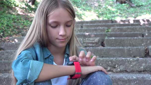 Szúró néz, gyermek használ SmartWatch szabadban történő-ban Park, gyerek játék-on smartphone — Stock videók