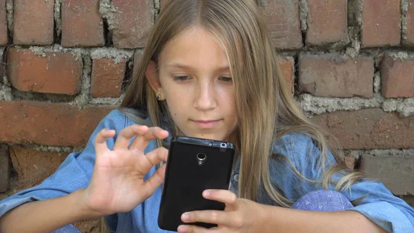 Barn som använder smartphone, Kid spelar på smart telefon, flicka utomhus i parken — Stockfoto