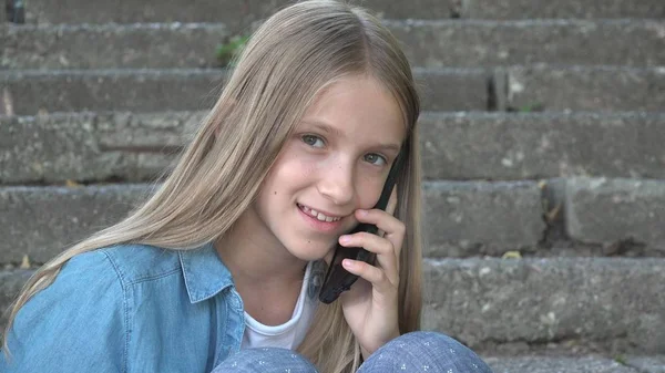 スマートフォンで話す子供、スマートフォンを使った子供、公園で屋外で遊ぶ女の子 — ストック写真