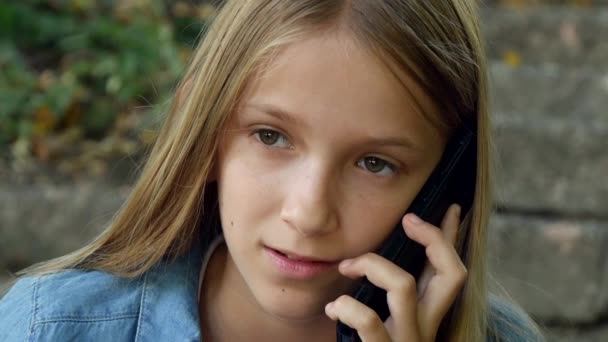 Ребенок разговаривает на смартфоне, ребенок с помощью смартфона, девушка играет на открытом воздухе в парке — стоковое видео