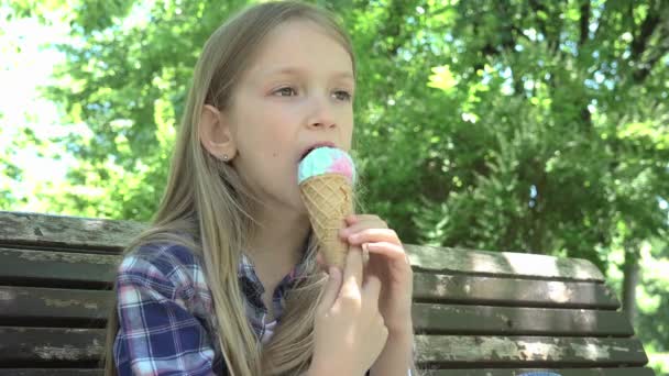Kid jíst zmrzlinu v parku, dítě relaxační sezení na lavičce dívka na hřišti — Stock video