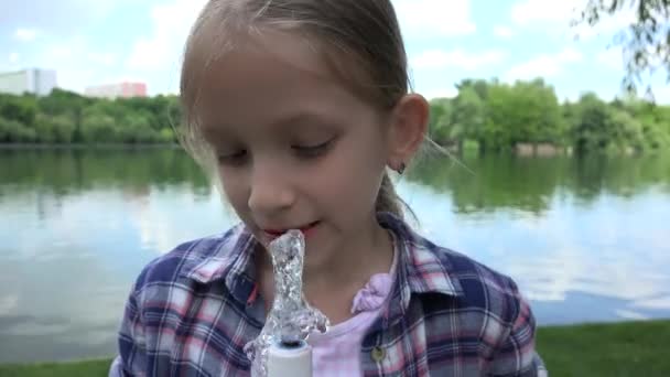 Ребенок пьет воду в парке, жаждущий детский портрет у фонтана, девушка играет на природе — стоковое видео