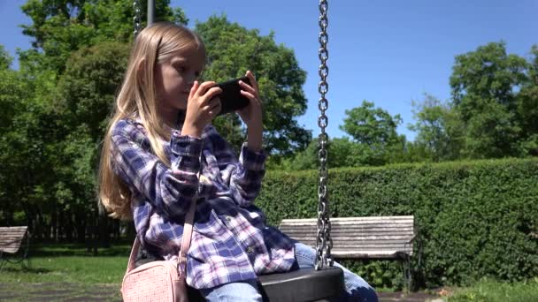 Kid Swinging Spela Tablet, Barn Bläddra Internet på smartphone Utomhus i Park, Flicka på Swing Använder Smartphone — Stockvideo