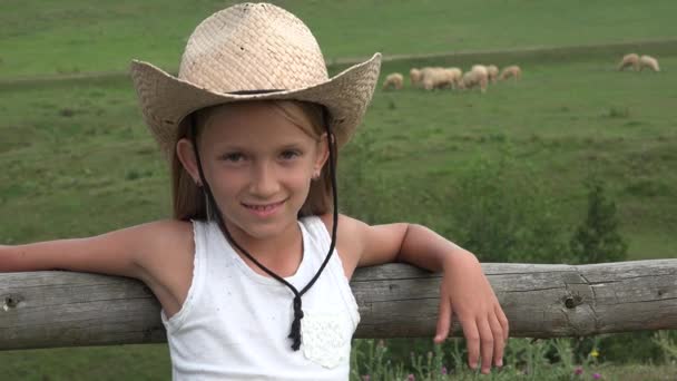 Детский портрет глядя, улыбаясь в камеру, ковбой ребенок с овцами пастбище, пастух в поле, счастливая девушка лицо играет на открытом воздухе 4K — стоковое видео