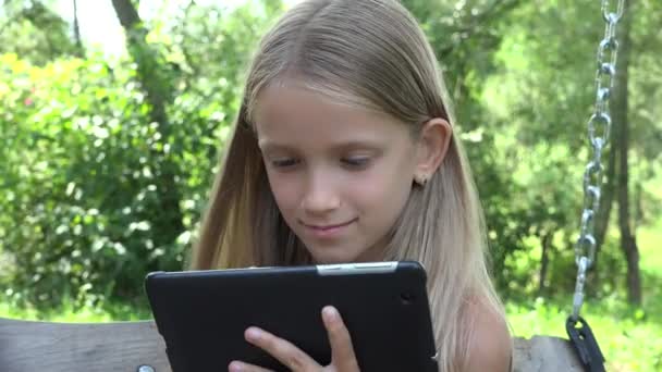 Качели на планшетных планшетах, просмотр детского интернета на устройстве на открытом воздухе во дворе сада, отдых девочек в природе — стоковое видео