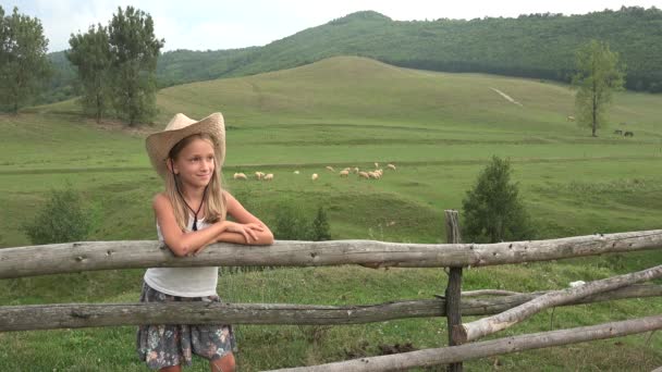 Kinderporträt gucken, in die Kamera lächeln, Cowboykind mit Schafen grasen, Hirte auf dem Feld, glückliches Mädchengesicht beim Spielen im Freien 4K — Stockvideo