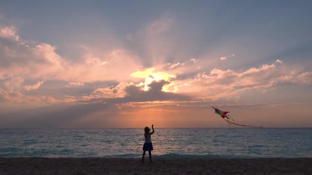 Kölyök játszik a tengerparton, gyermek repülő sárkány naplementekor az óceánon, kislány a tengerparton a nyári vakáció — Stock videók