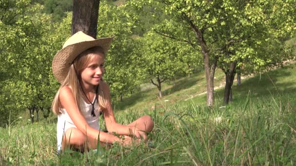 Kind spielt im Gras, gelangweiltes Kind entspannt sich im Obstgarten im Freien, nachdenkliches blondes Mädchen in der Natur — Stockvideo