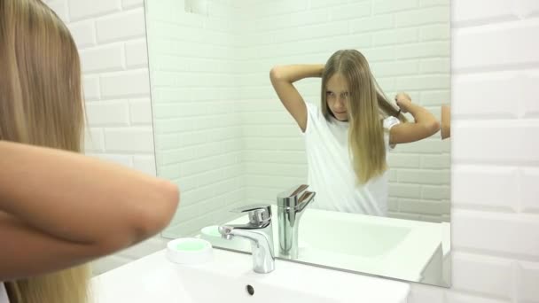 Ребенок расчесывает волосы в зеркале, ребенок причесывается в ванной, блондинка расчесывается, прическа — стоковое видео