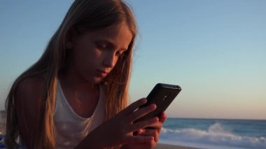 Akıllı Telefon Oynayan Çocuk, Gün Batımında Sahilde Çocuk, Yaz Tatili 'nde Gün batımında Deniz kenarında Tablet Kullanan Genç Sarışın Kız