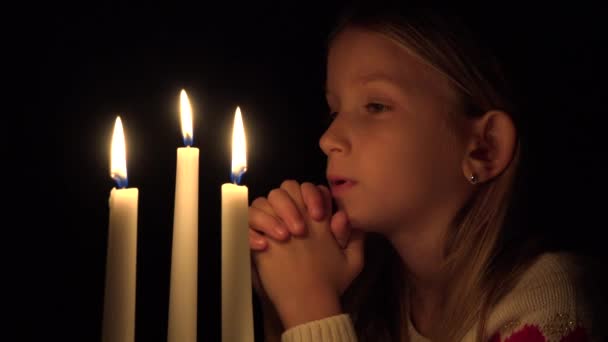 Грустный ребенок молится при свечах Свет, несчастный ребенок портрет молится ночью, религиозный вдумчивый блондинка медитирует в темноте — стоковое видео
