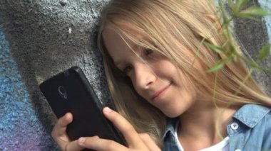 Çocuk parkta akıllı telefonda oynuyor, çocuk akıllı telefonda internete bakıyor, sarışın ergen kız cihazda mesajlar yazıyor.