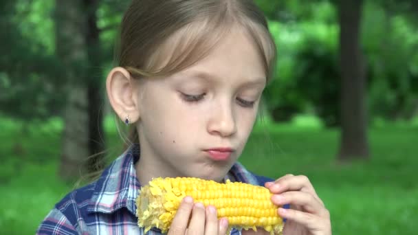 Criança comendo milho cozido ao ar livre no parque, garota faminta come comida saudável, criança loira jovem relaxante ao ar livre na natureza — Vídeo de Stock