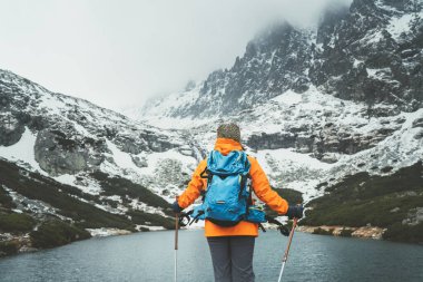 Slovakya 'nın başkenti Velicka Vadisi' nde dağ yürüyüşü sırasında Velicke pleso (dağ gölü) manzarasının tadını çıkaran, yürüyüş direkleri olan parlak turuncu ceketli bayan sırt çantalı. Etkin insanlar konsepti