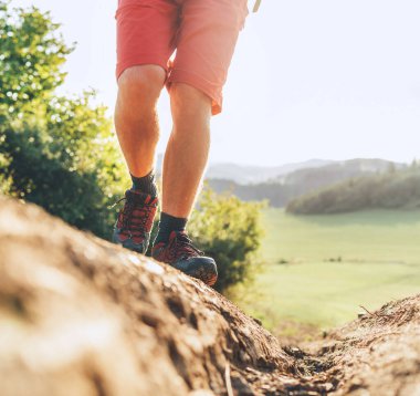 Yazın güneşli bir günde, dağda kirli patikada yürüyüş botlarıyla gezen sırt çantalı gezgin ayaklarını kapat.