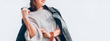 Gülümseyen moda tarzı, sıcak örgü süveter, siyah deri motosiklet ceketi ve beyaz arka planda moda güneş gözlüklü Beanie Hat..