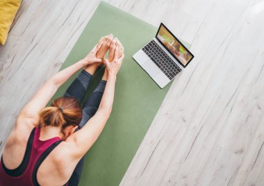 Paschimottanasana pozunda oturan sportif sağlıklı bir kadın, nefes egzersizleri yapıyor, dizüstü bilgisayarda online yoga dersleri izliyor. Sağlıklı insanlar ve motivasyon Top view konsepti.