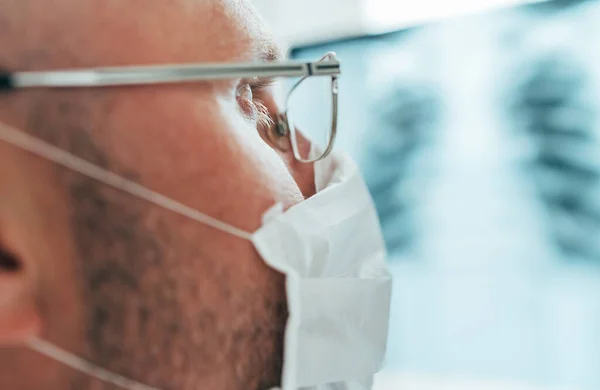 Close up shoot of Male doctor's eye with eyeglasses examining the patient chest x-ray film lungs scan at radiology department in a hospital. Human body medical or Respiratory tract infection concept.